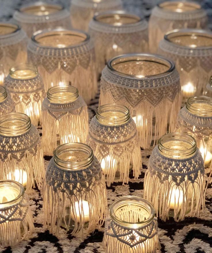 many small glass jars with candles in them sitting on a tablecloth covered floor next to each other