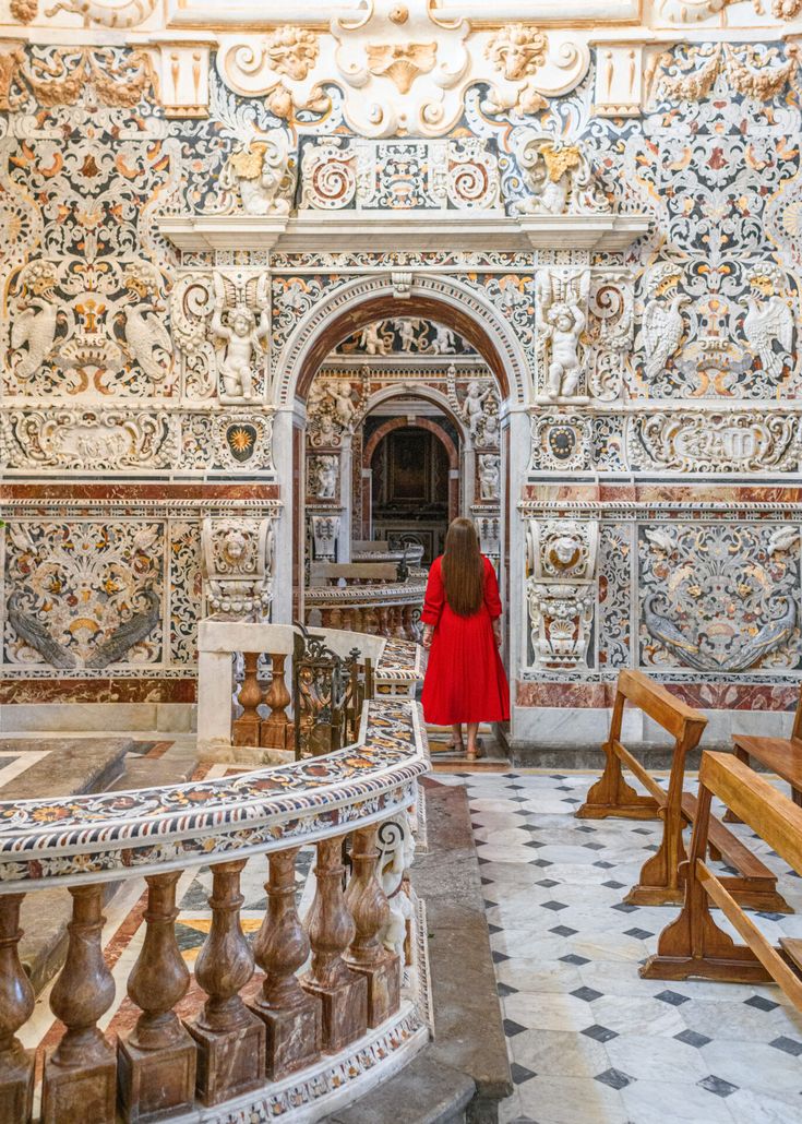 a woman in a red coat is walking through an ornately decorated room with wooden benches