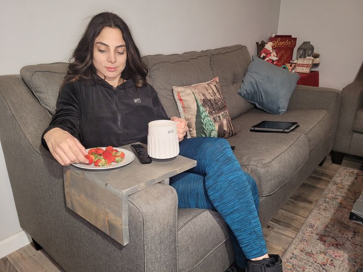 a woman sitting on a couch with a plate of fruit and coffee in front of her