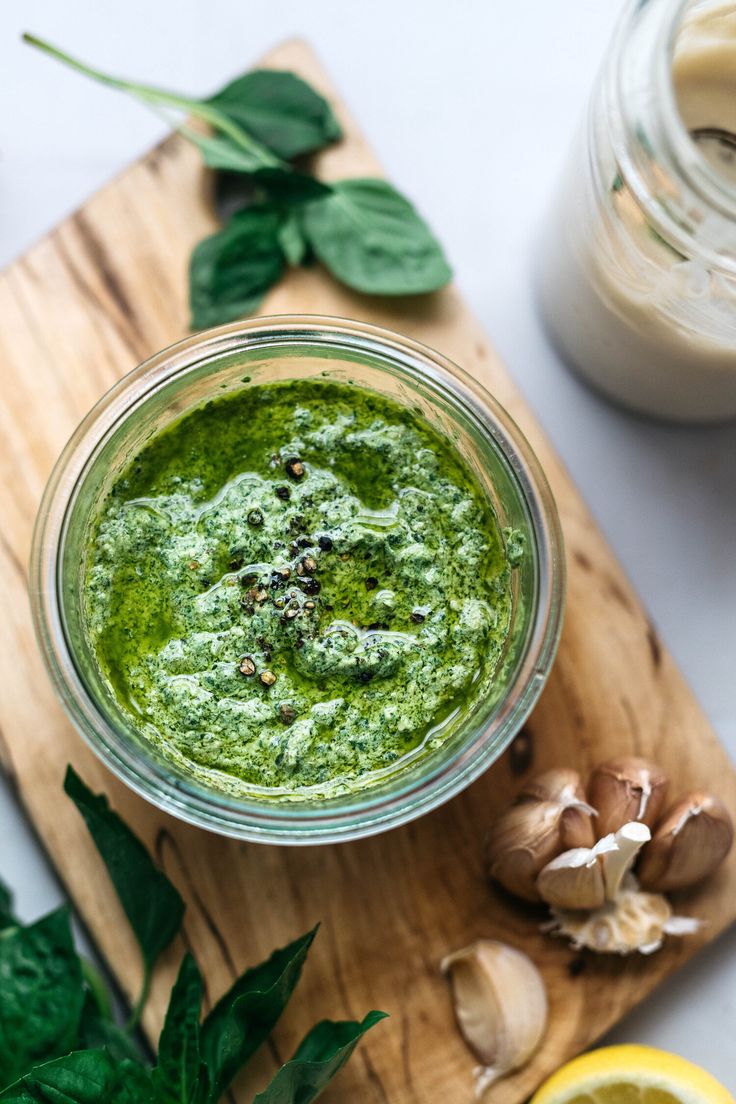 a glass jar filled with green pesto next to sliced lemons and garlic on a cutting board