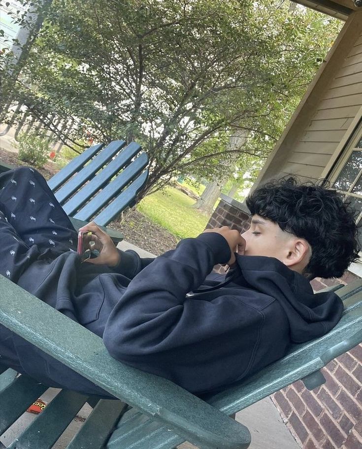 a young boy laying on top of a green bench next to a blue chair and tree