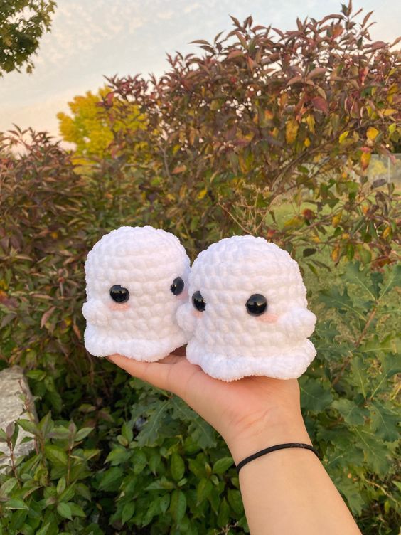 two small crocheted sheeps are held up in front of some shrubbery