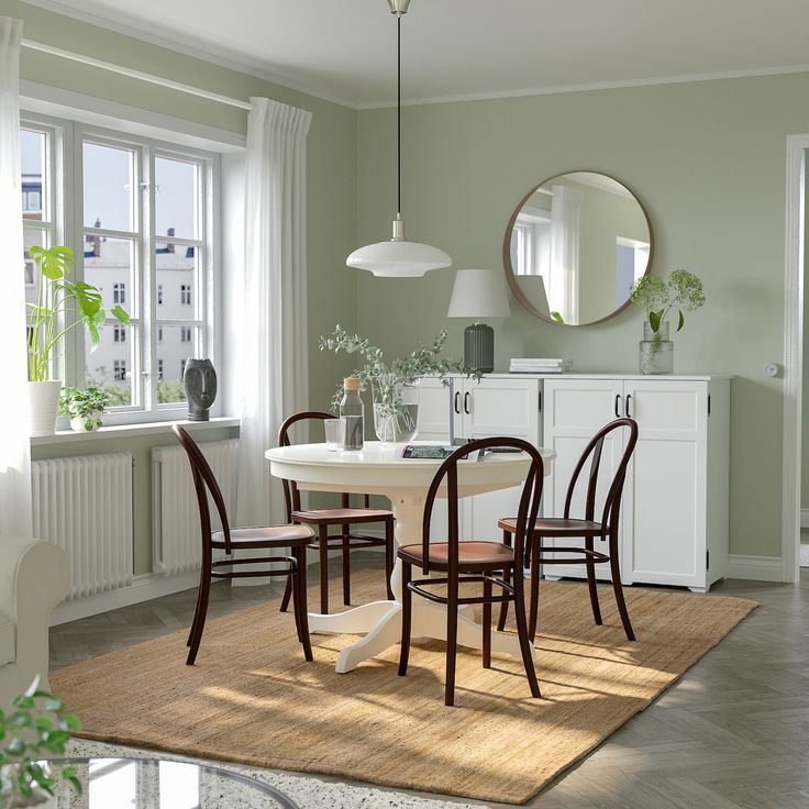 a dining room table with chairs and a round mirror on the wall above it in front of a window