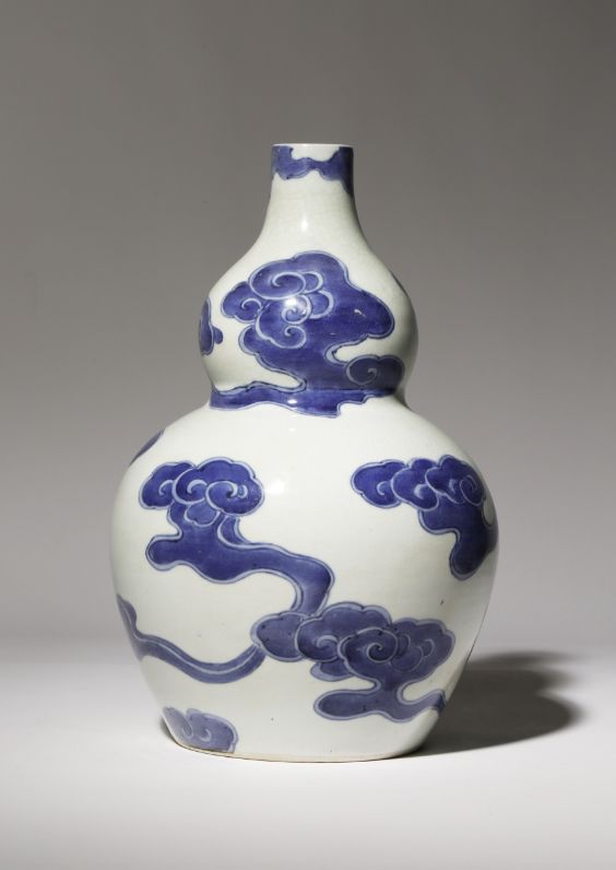 a blue and white vase with clouds on it's body, sitting in front of a gray background