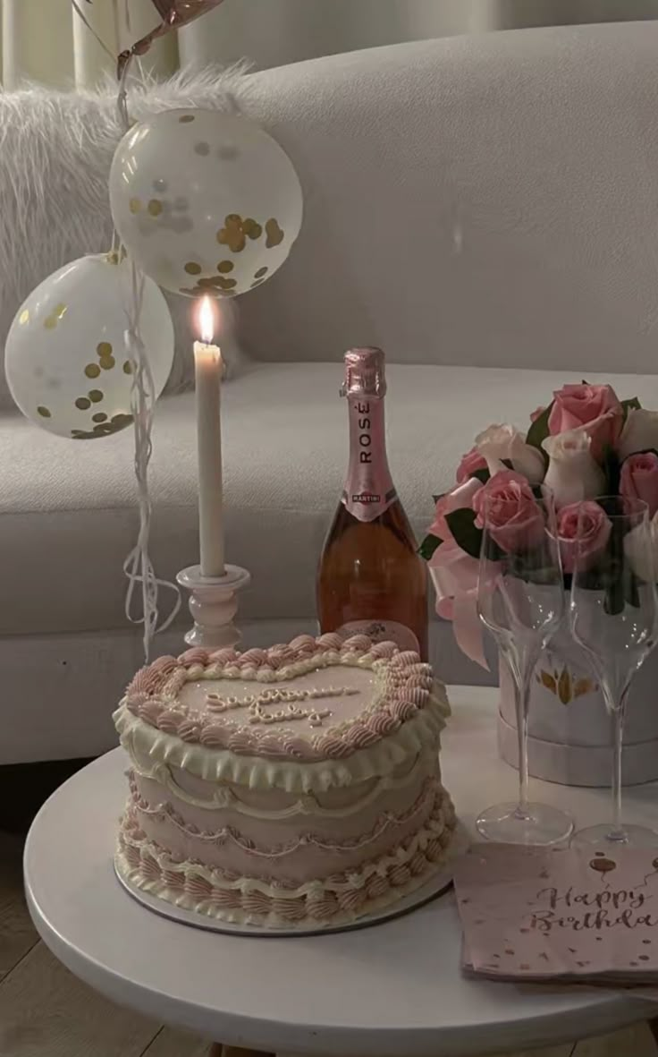 a table topped with a cake next to a bottle of wine and glasses filled with pink roses