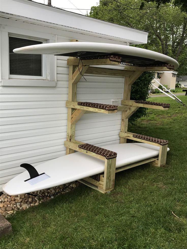 a white surfboard sitting on top of a wooden shelf in front of a house