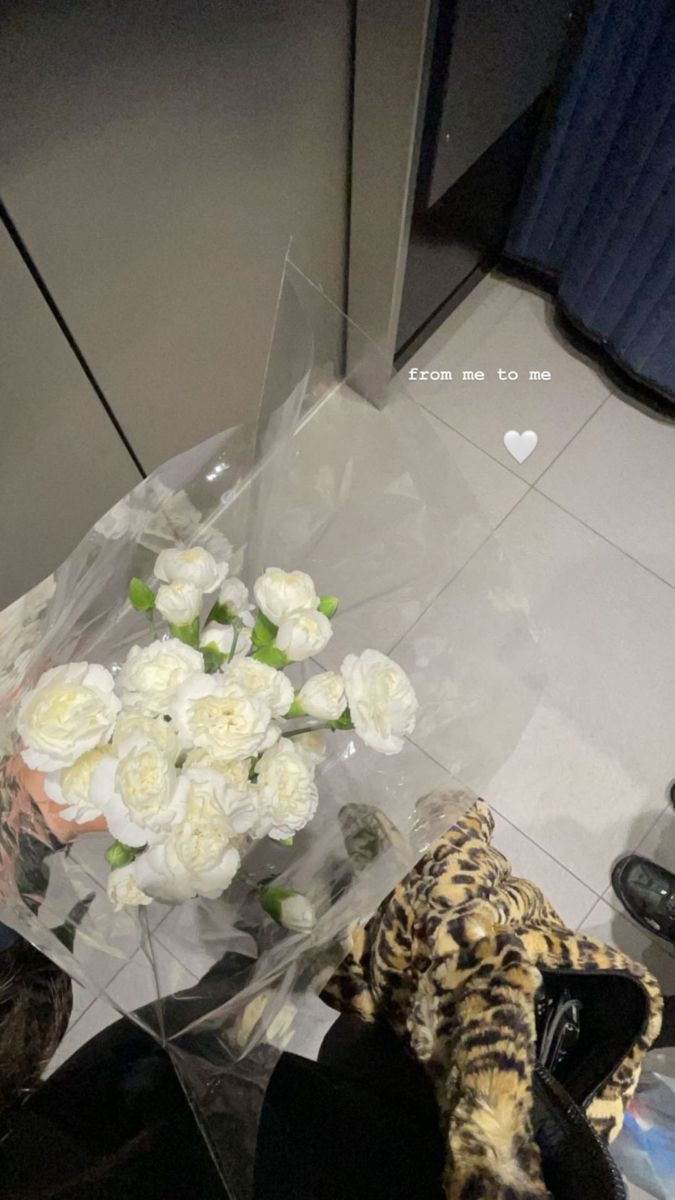 a bouquet of white roses in a clear plastic bag on the floor next to a pair of black shoes