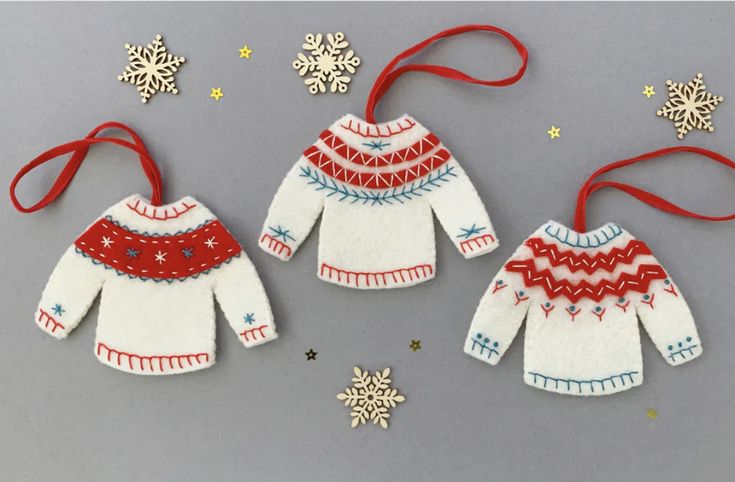 two knitted sweaters ornament hanging from a red ribbon next to snowflakes