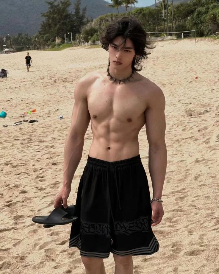 a shirtless young man standing on the beach