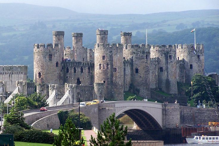 an old castle with a bridge going over it and lots of trees in the foreground