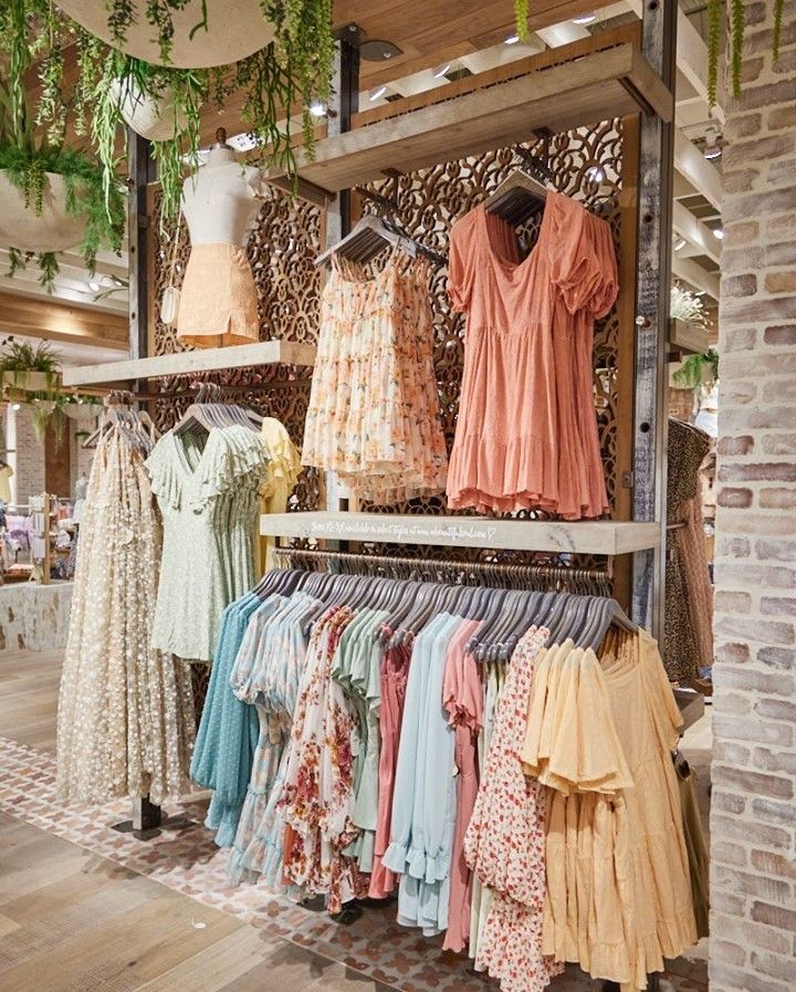 clothes are on display in a store with brick walls and wooden floors, along with hanging plants