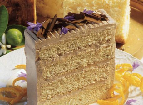 a piece of cake sitting on top of a white plate next to orange slices and flowers