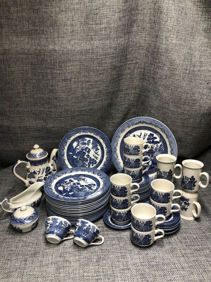 a pile of blue and white china sitting on top of a gray cloth covered couch