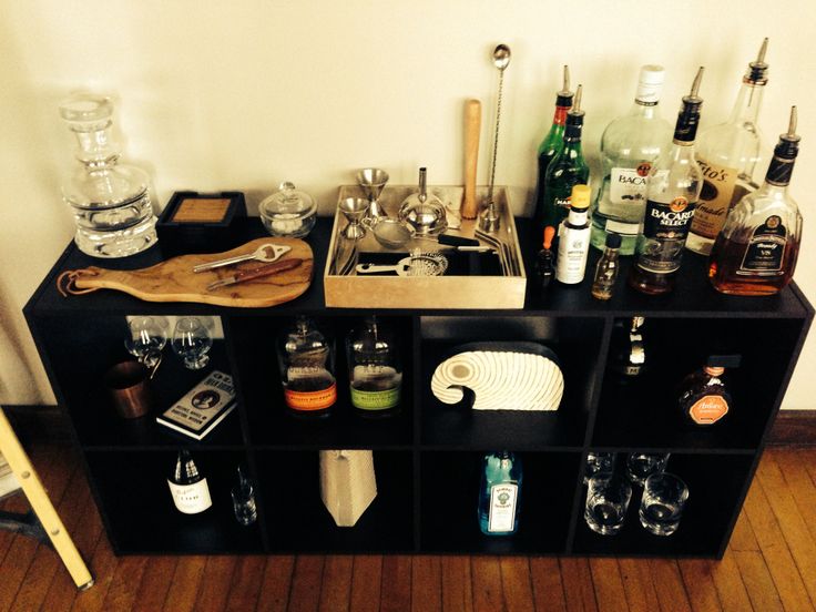 an assortment of liquor bottles and glasses sitting on top of a black bookcase next to a wooden floor