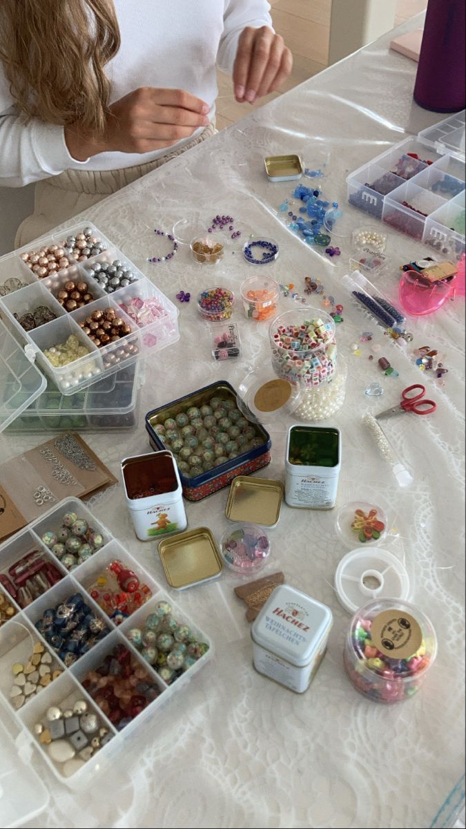 a woman sitting at a table with lots of beads and other items on the table