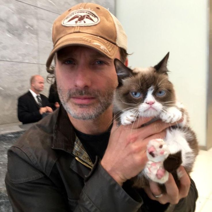 a man holding a cat in his right hand and wearing a hat on top of his head