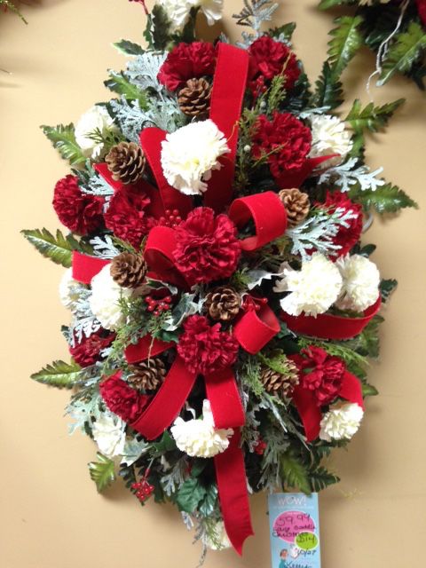 a christmas wreath with red and white flowers, pine cones and evergreens is hanging on the wall