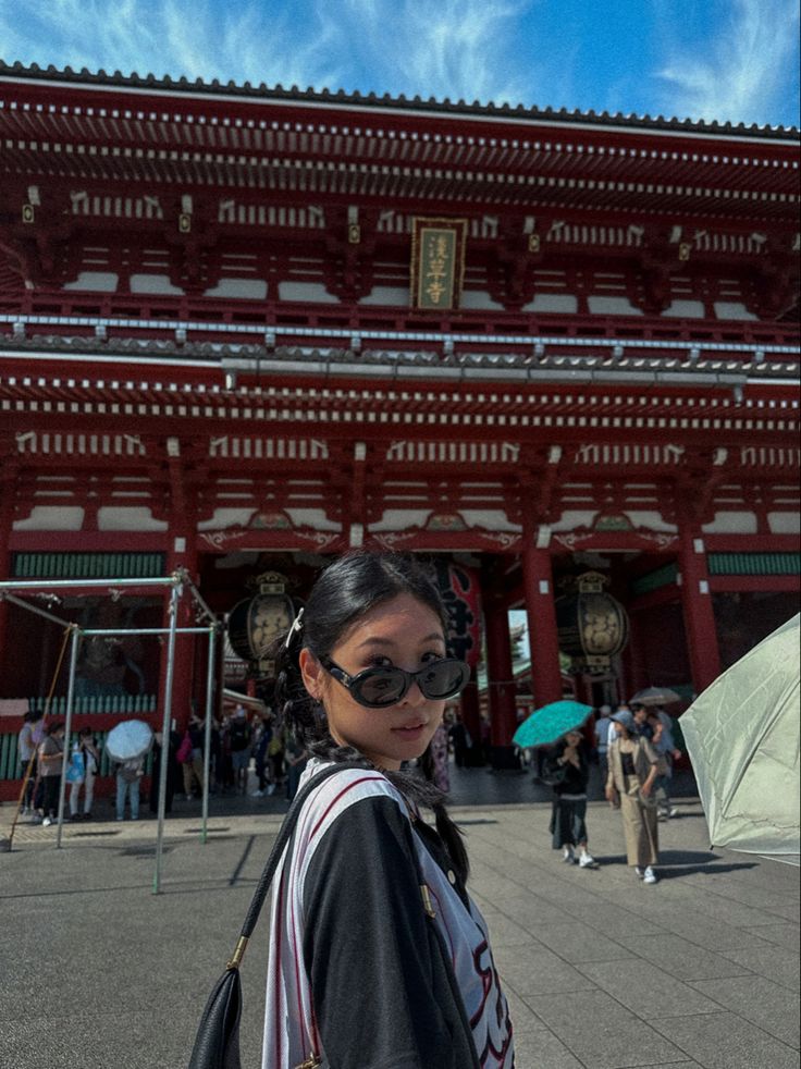 a woman standing in front of a building with an umbrella over her head and wearing sunglasses