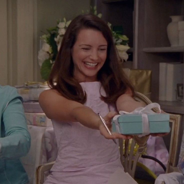 two women sitting at a table and one is holding a blue box with a bow on it