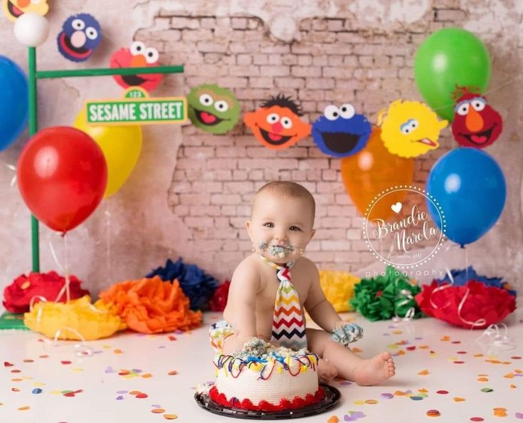 a baby sitting in front of a cake with balloons and sesame street signs on it