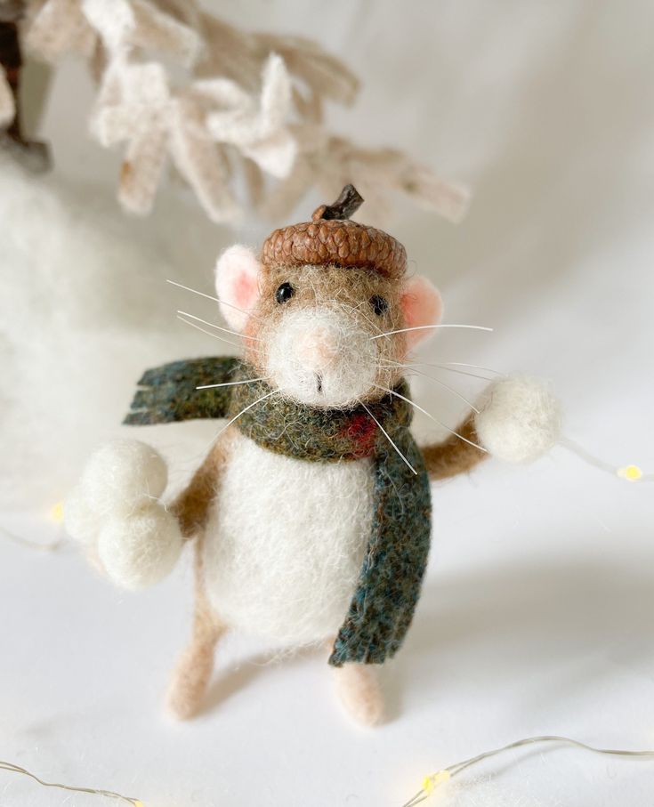 a needled mouse with a hat and scarf on it's back, standing in front of christmas lights