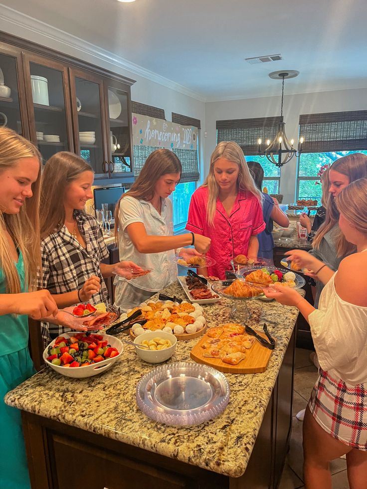 a group of women standing around a kitchen counter preparing food