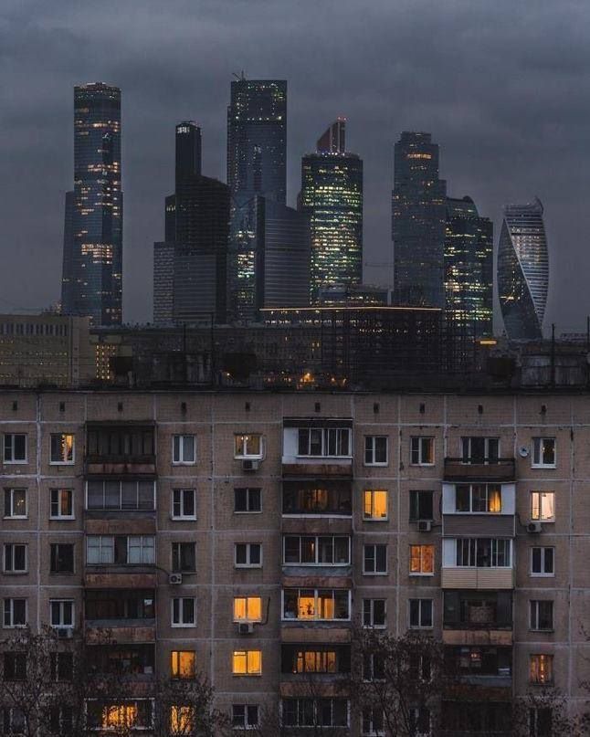 the city skyline is lit up at night, with buildings in the foreground and dark clouds overhead