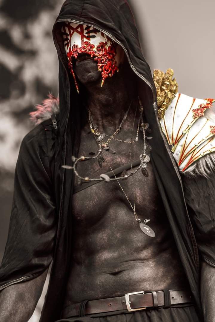 a man with his face covered in black and gold jewelry, wearing a hoodie