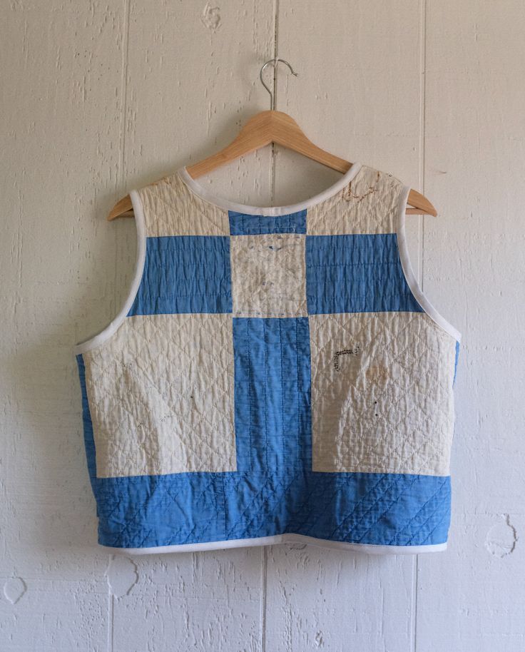 a blue and white quilted top hanging on a wooden hanger against a wall