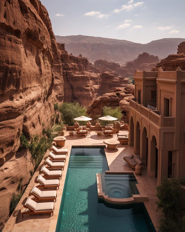 an outdoor swimming pool with chaise lounges and mountains in the background