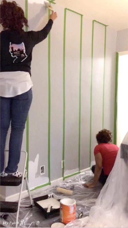 two women are painting the walls in a room that is being remodeled with green tape