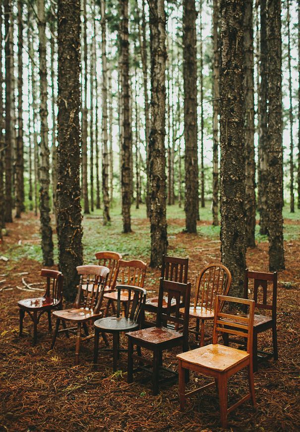 several wooden chairs and tables in the middle of a forest with tall trees behind them