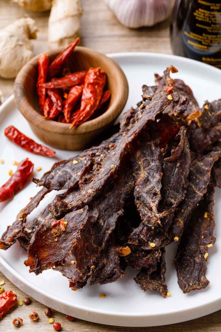 a white plate topped with beef strips next to garlic and peppers