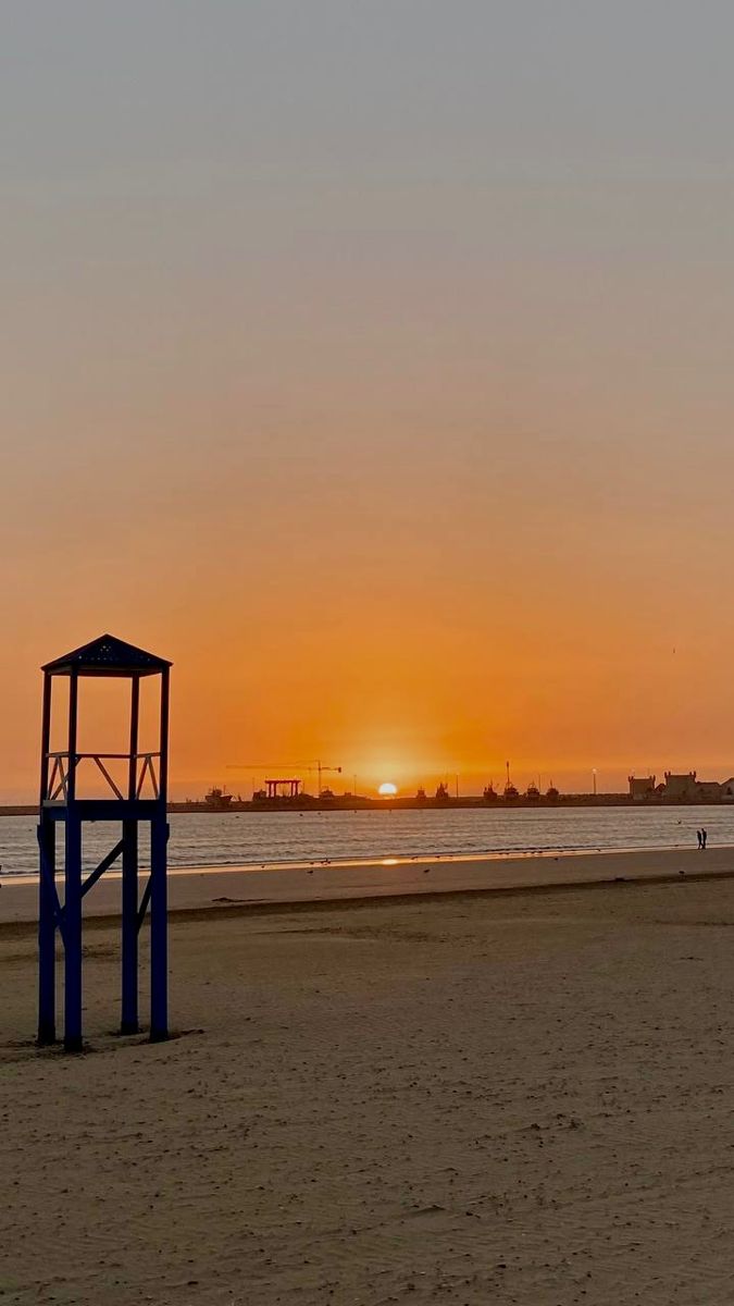 the sun is setting at the beach with people on it