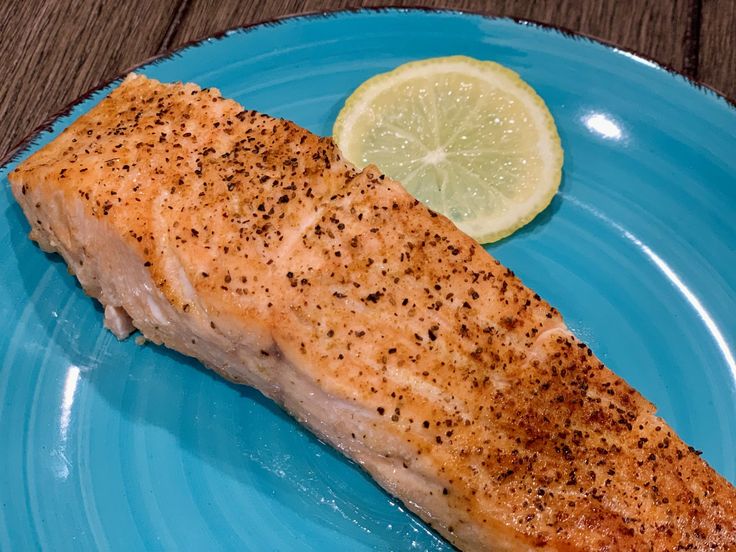 a piece of salmon on a blue plate with a lemon wedge