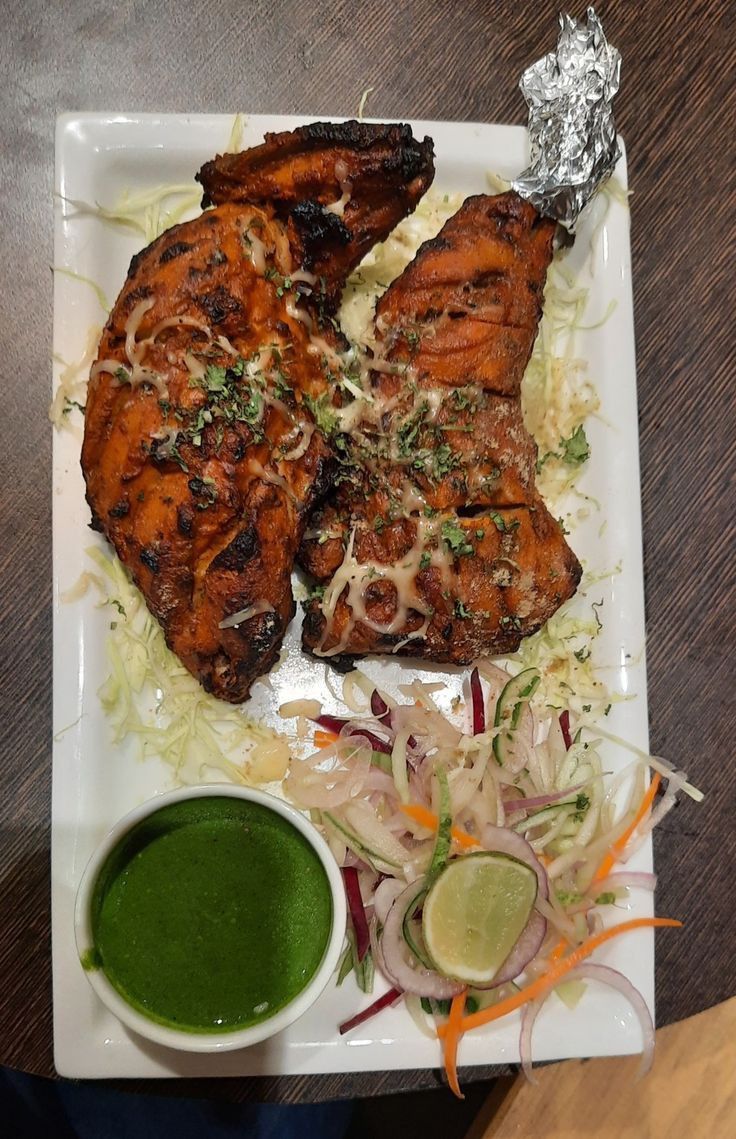 two pieces of meat and some vegetables on a white plate with green sauce next to it