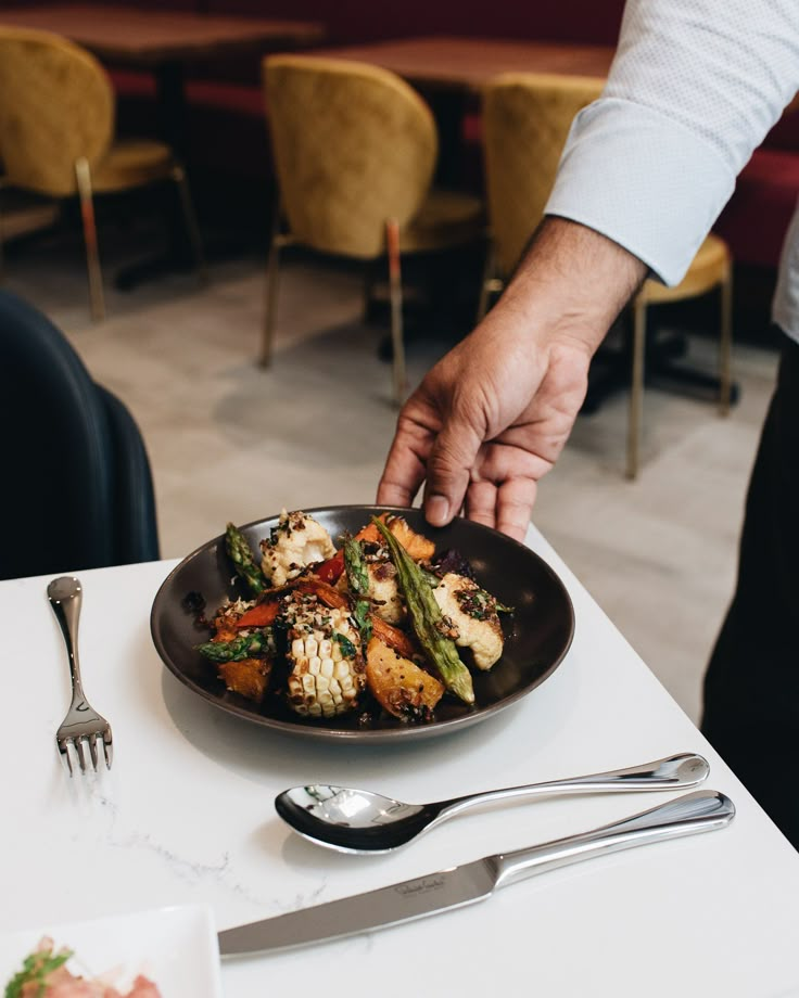 a person reaching for food in a plate on a table with silverware and utensils