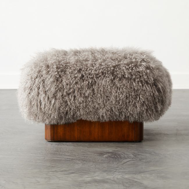 a furry stool on a wooden stand in front of a white wall and grey floor