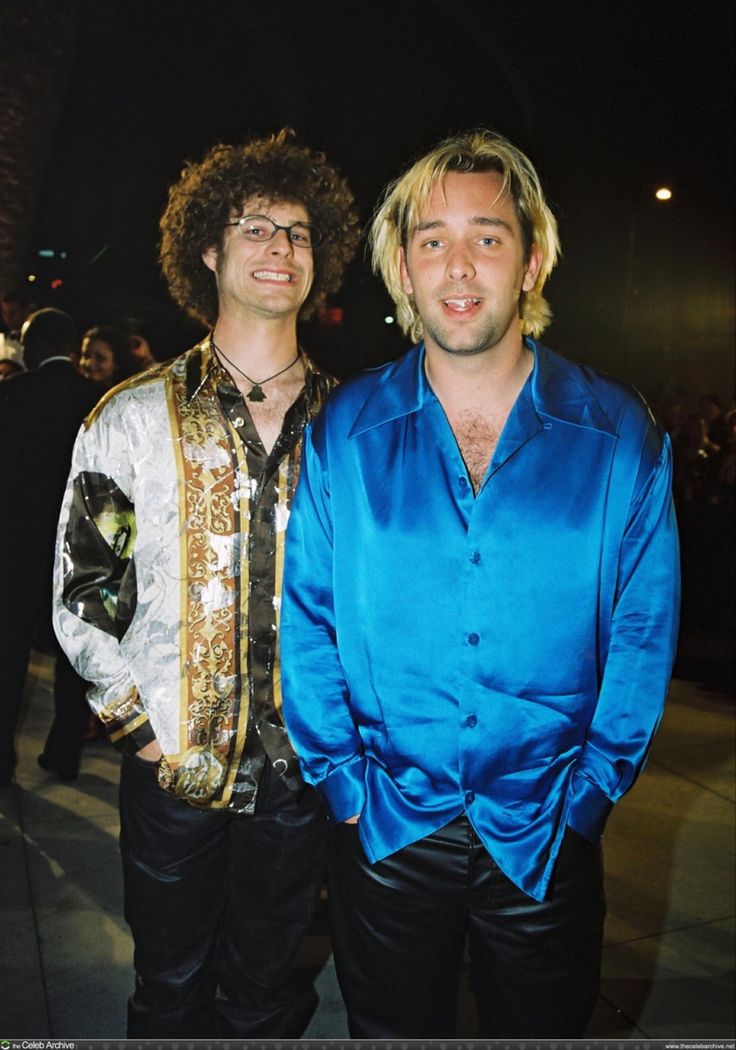 two men standing next to each other in front of a crowd at an event, one wearing a blue shirt and the other black pants