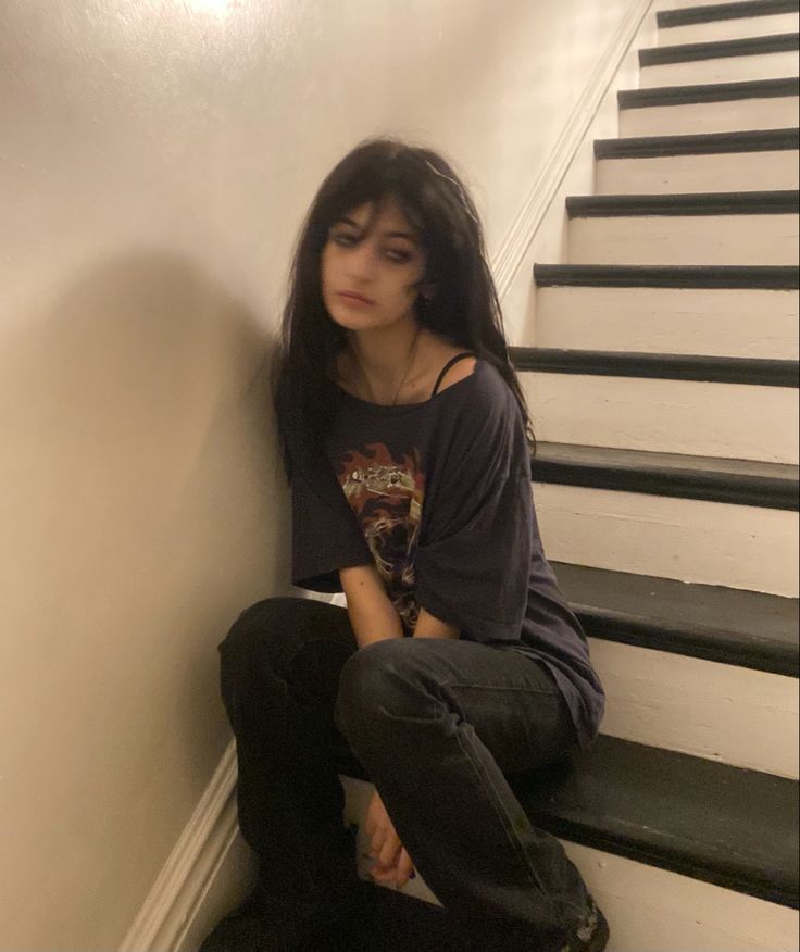 a young woman sitting on the stairs with her hands in her pockets and looking down