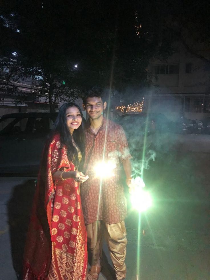 a man and woman standing next to each other holding sparklers in their hands at night