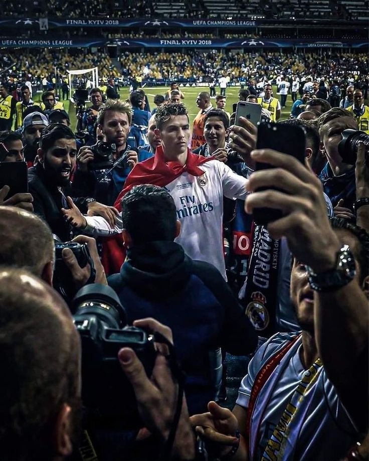 a group of people standing around each other at a soccer game, taking pictures with their cell phones