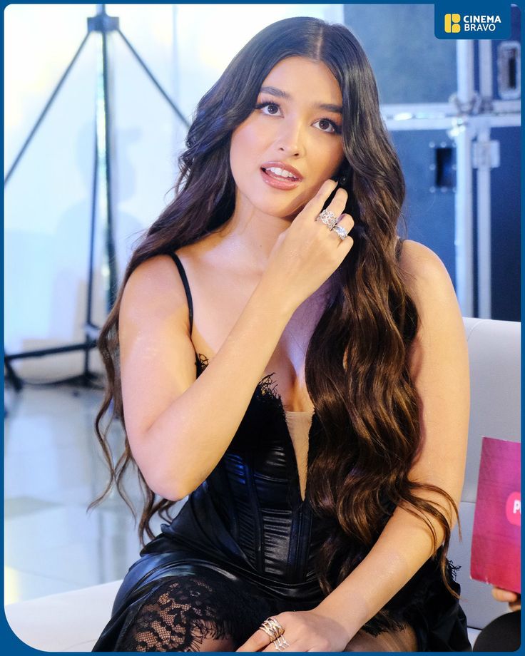 a woman sitting on top of a white couch wearing a black dress and holding her hand up to her face