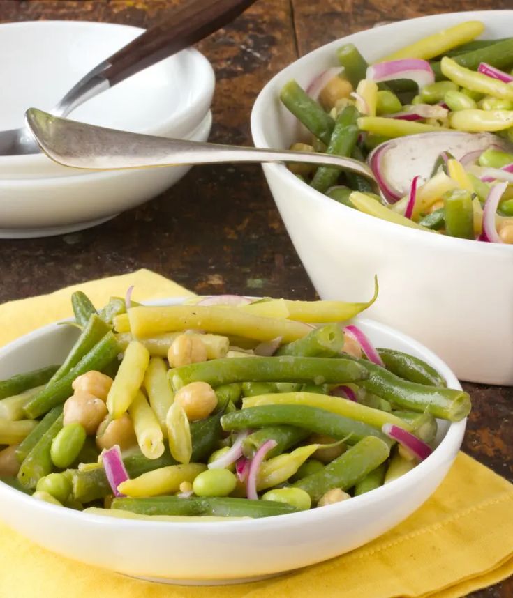 two bowls filled with green beans, onions and other vegetables on top of a yellow napkin