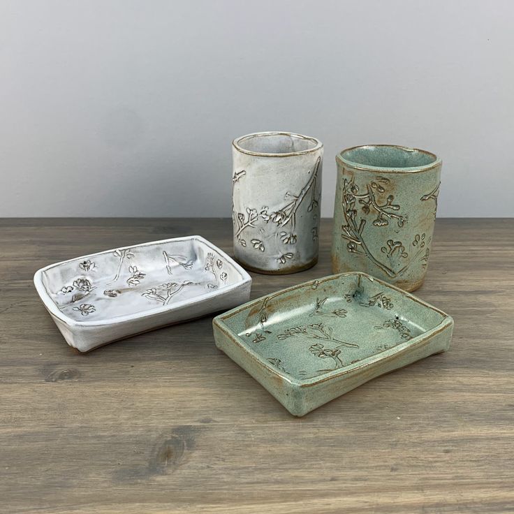 three pieces of pottery sitting on top of a wooden table next to a cup and saucer