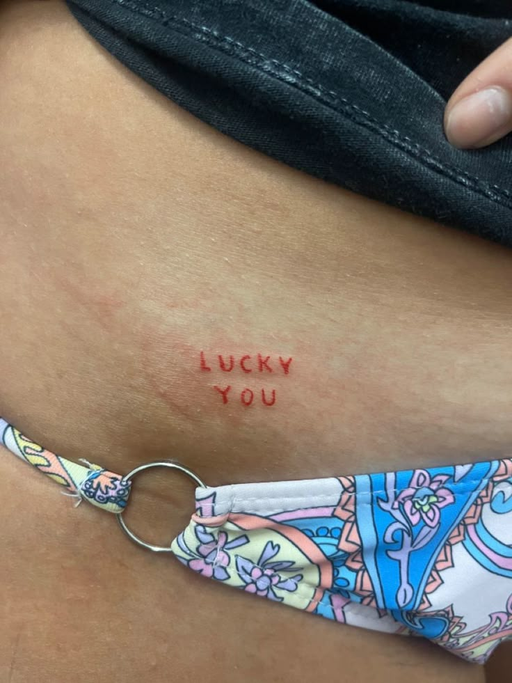 a woman's stomach with the words lucky you tattooed on her lower side belly