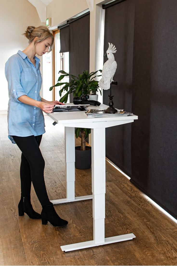 a woman standing at a white table with a plant on it and an electronic device in front of her