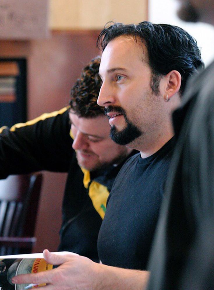 two men are sitting at a table and one is holding a remote control in his hand