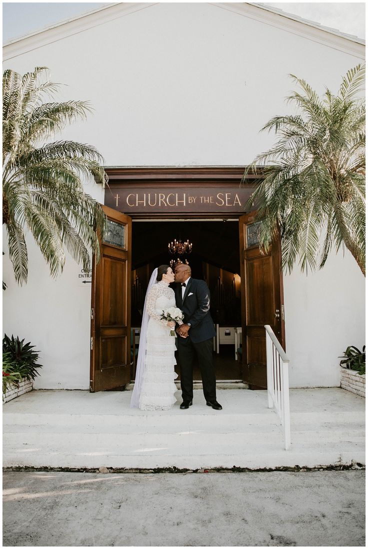 a bride and groom standing in front of the church of the sea with palm trees