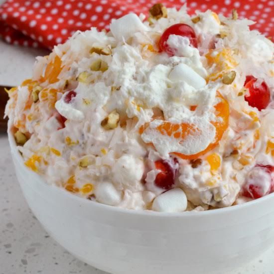 a white bowl filled with fruit salad on top of a table next to a red and white napkin